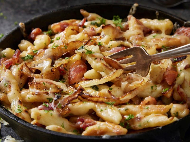 Eine Pfanne Miso-Spätzle mit karamellisierten Zwiebeln und Kräutern, darin eine Gabel.