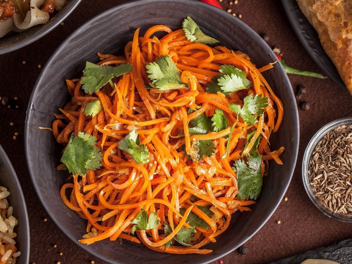 Ein Teller Morkowtscha, koreanischer Möhrensalat, mit Korianderblättern in der Draufsicht.