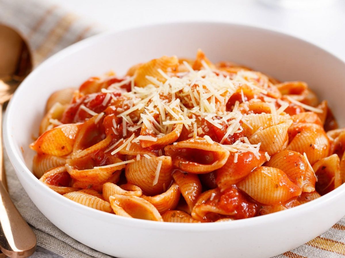 Eine Schüssel Pasta mit gerösteter Tomatensauce und etwa Käse, daneben ein Löffel und eine Gabel.