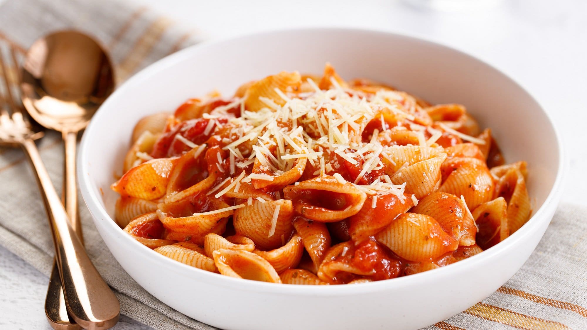 Eine Schüssel Pasta mit gerösteter Tomatensauce und etwa Käse, daneben ein Löffel und eine Gabel.