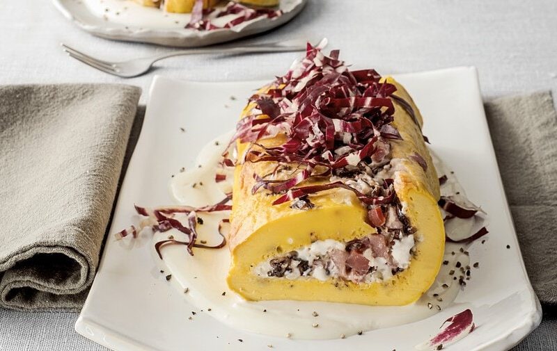 Pikante Biskuitroulade auf einem weißen Teller vor hellem Hintergrund.