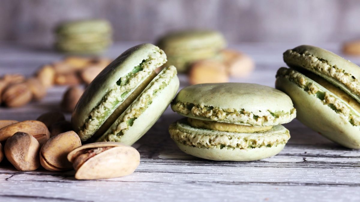 Pistazien-Macarons neben Pistazien vor hellem Hintergrund.