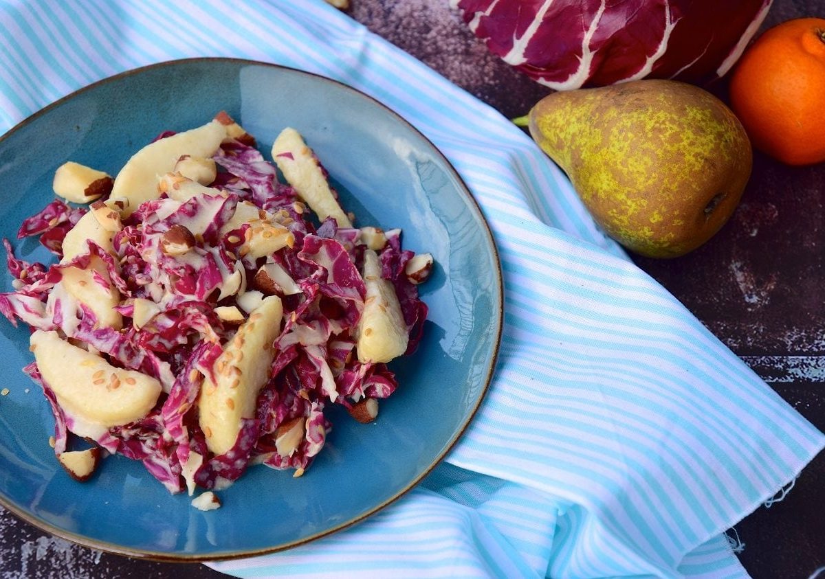 Draufsicht: ein Teller Radicchio-Salat mit Birnen und Paranüssen. Daneben liegen ein Raddichio, eine Birne und eine Orange.