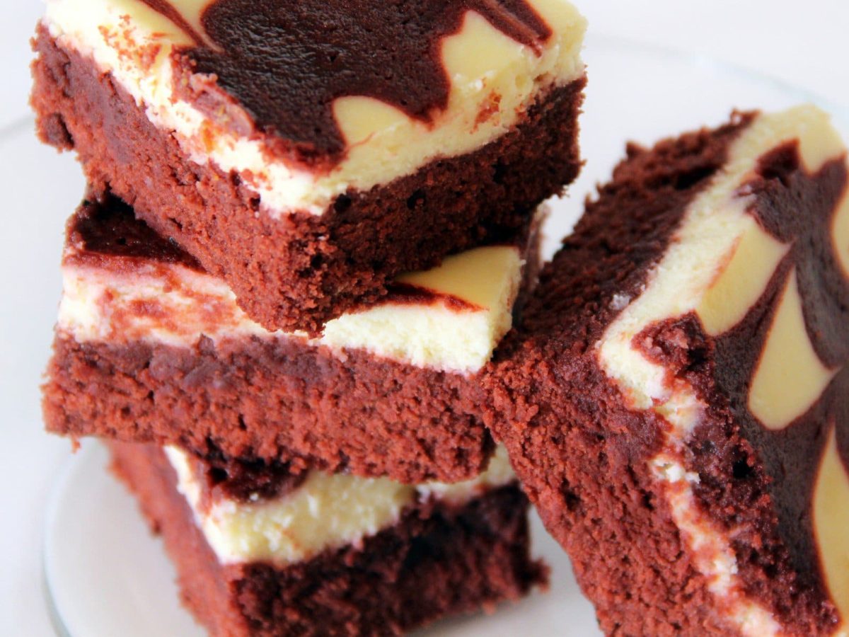 Red Velvet Brownies mit Vanilla-Icing gestapelt auf weißem Teller. Draufsicht.