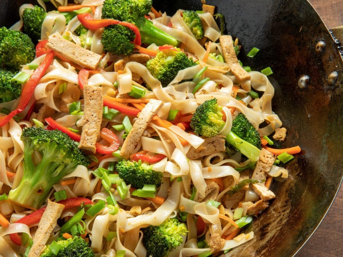 Ein schwarzer Wok mit dem Reisband-Nudelsalat auf einem dunklen Holztisch.