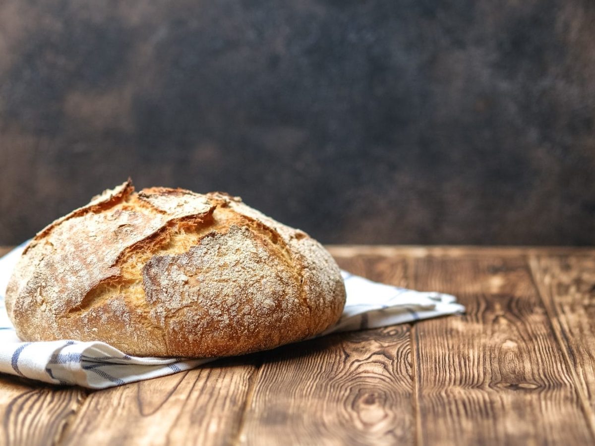 Selbst gebackenes Krustenbrot auf Tuch und Holztisch. Frontalansicht.