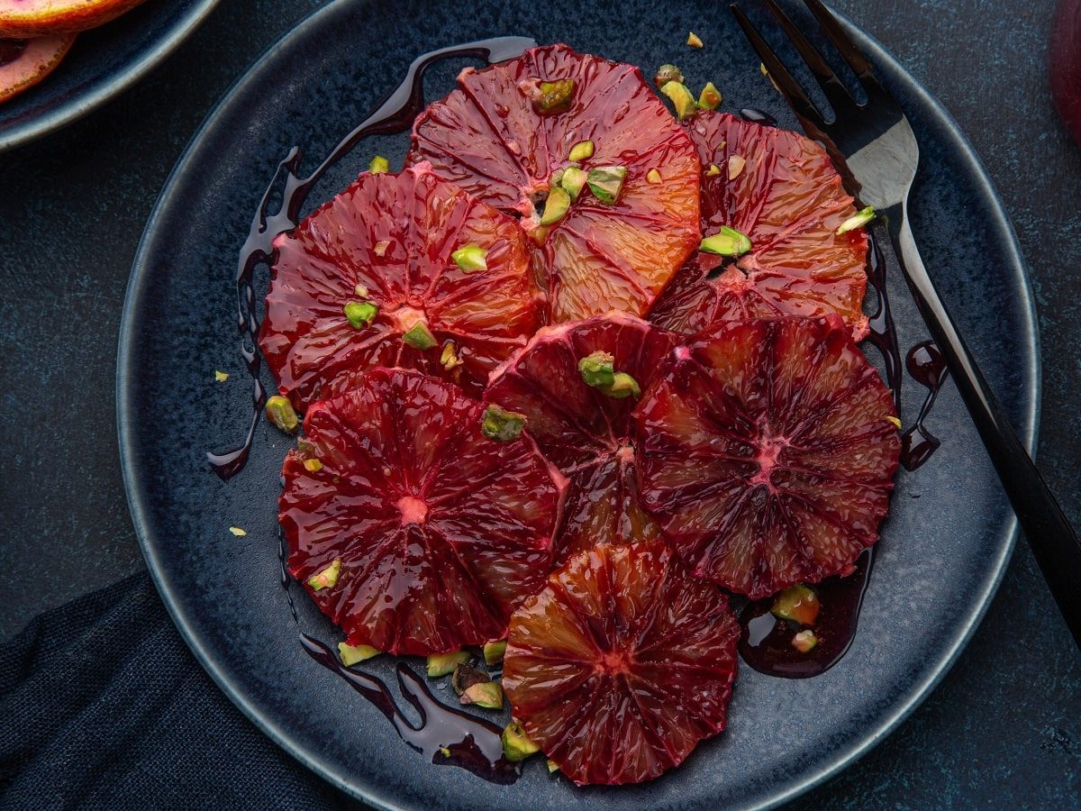 Ein schwarzer Teller mit Blutorangen-Carpaccio mit gerösteten Pistazien.