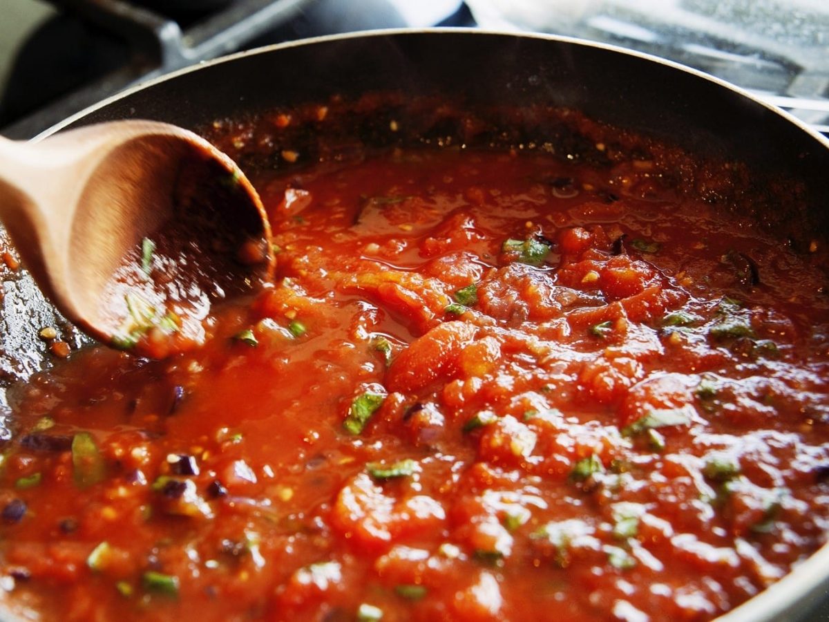 Spaghetti Pomodoro, köchelnd in einer großen, tiefen Pfanne, garniert mit frischem Basilikum und umgerührt mit einem Holzlöffel.