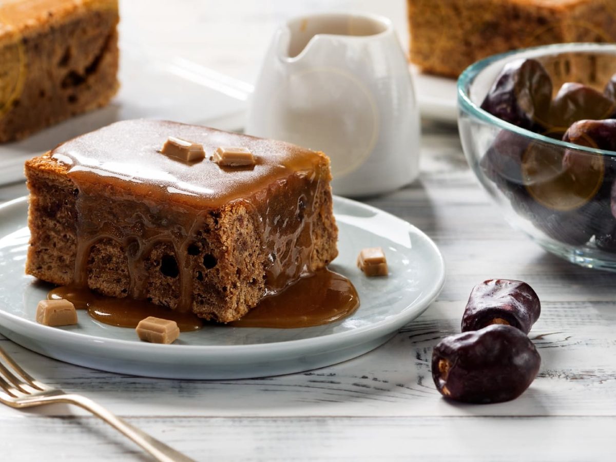 Toffee Pudding auf einem weißen Tisch mit einer Glasschale Datteln.