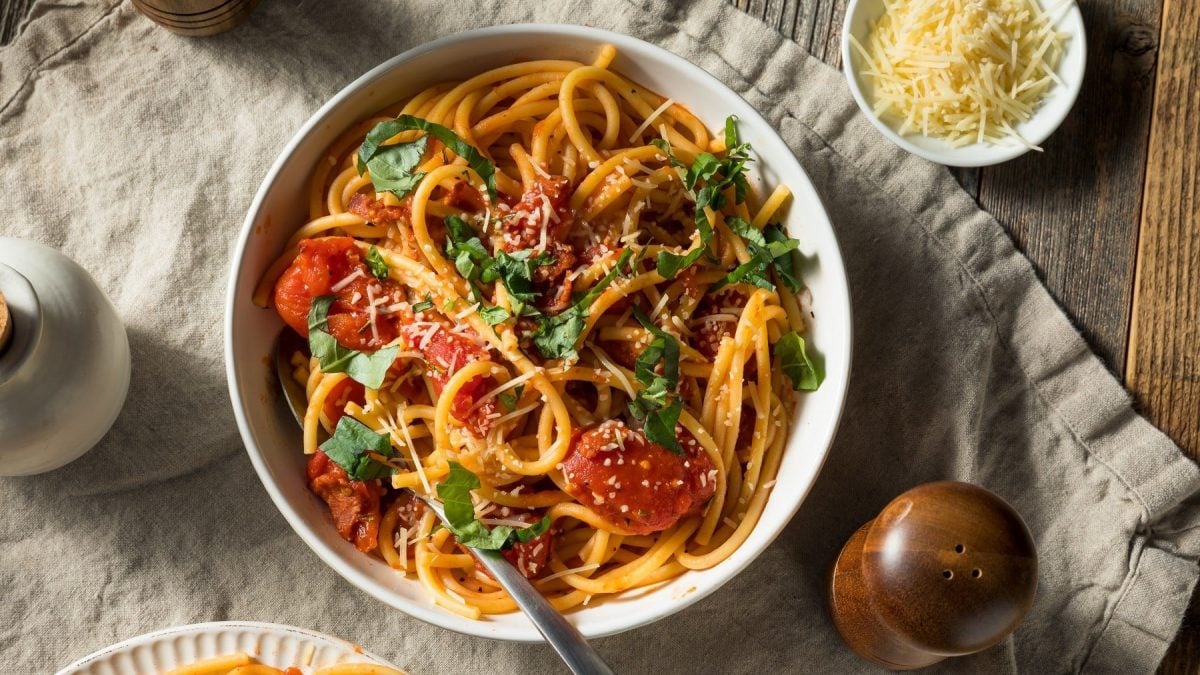 Vegane Pasta all'Amatriciana, garniert mit frischem Basilicum und geriebenem veganen Käse in einer großen, weißen Schale.