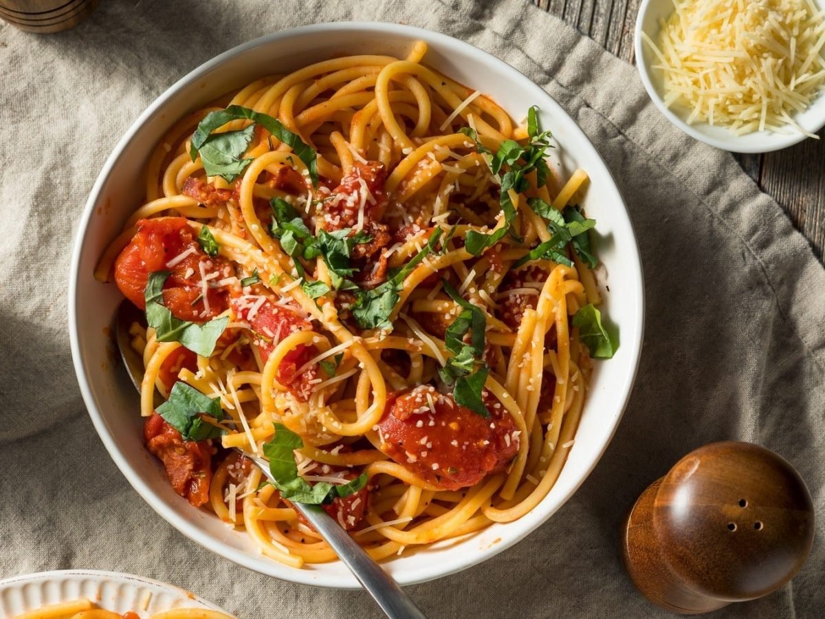 Vegane Pasta all'Amatriciana, garniert mit frischem Basilicum und geriebenem veganen Käse in einer großen, weißen Schale.