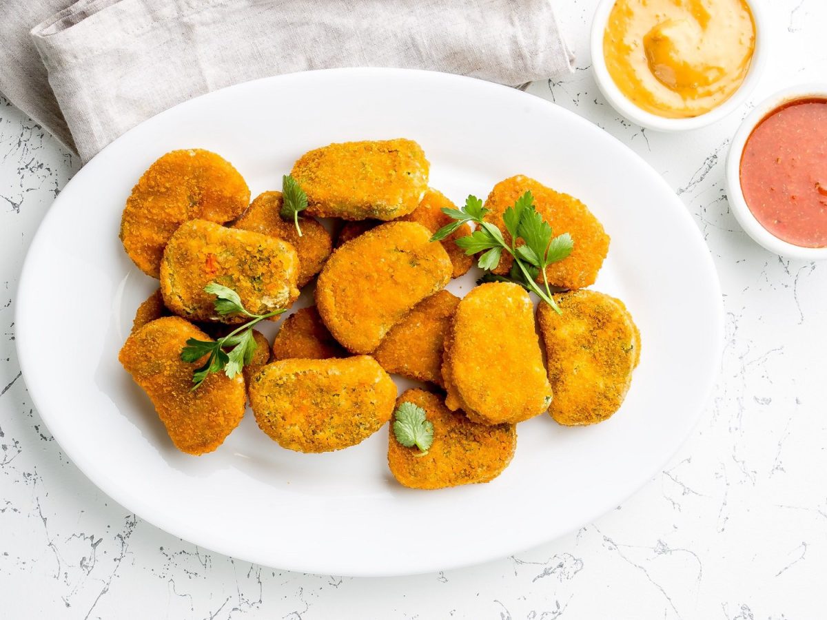 Ein TellerTofu Nuggets mit einem Schälchen eines weißen Dips, bestreut mit Petersilie, daneben zwei Dip-Schalen.