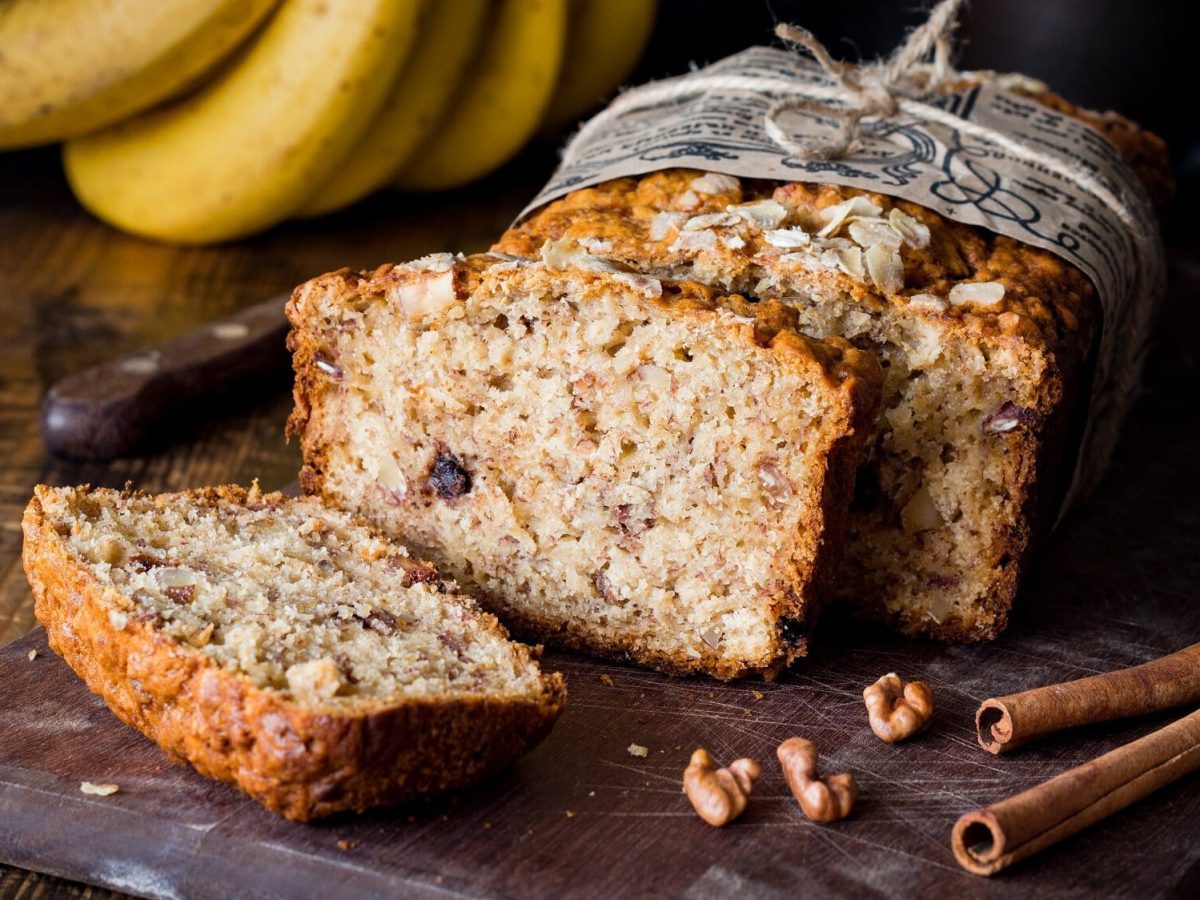 Ein angeschnittenes veganes Zimtbrot, daneben liegen Zimtstangen.