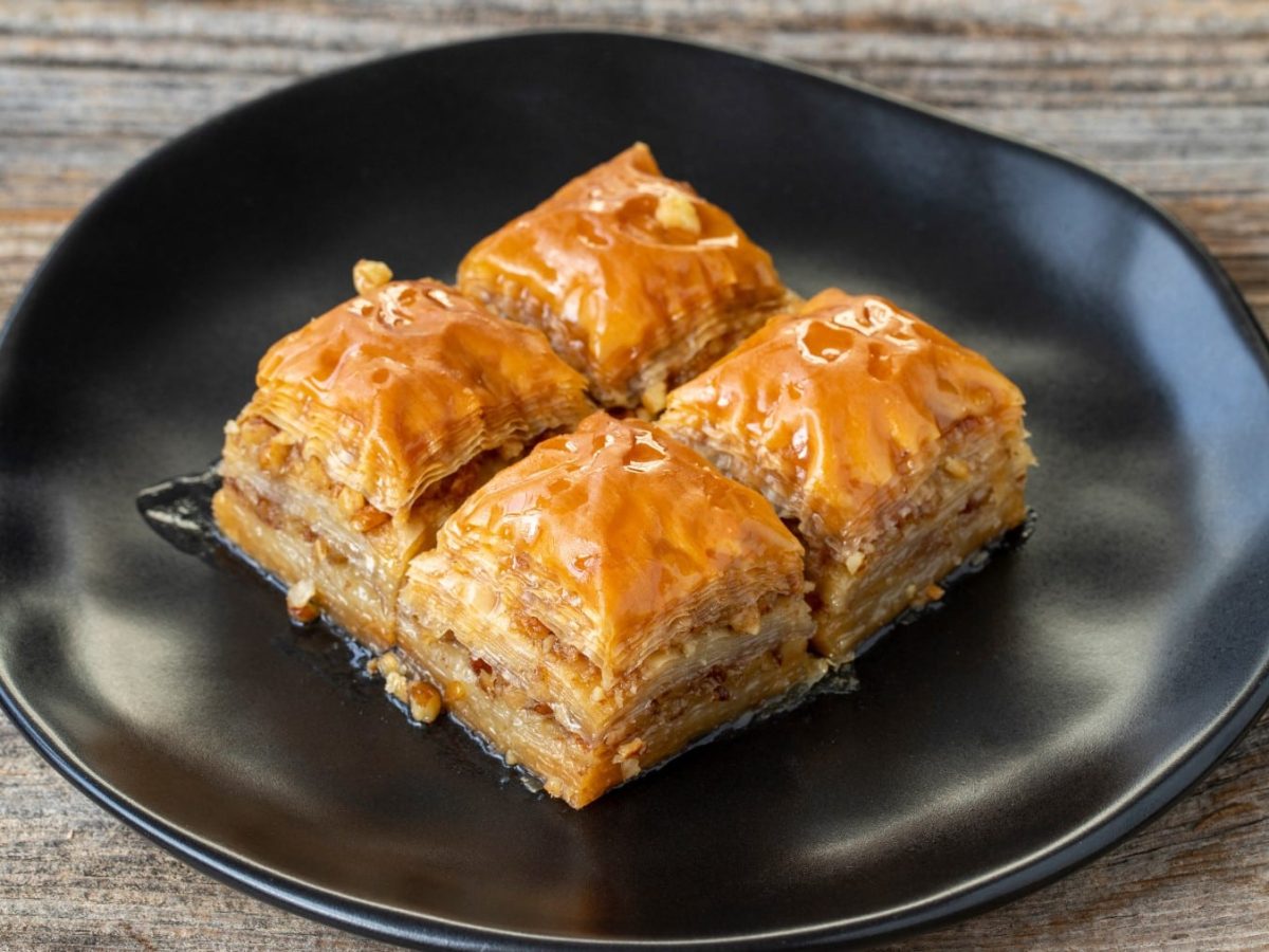 Vier Stücke Walnuss-Baklava auf einem schwarzen Teller auf Holzhintergrund.