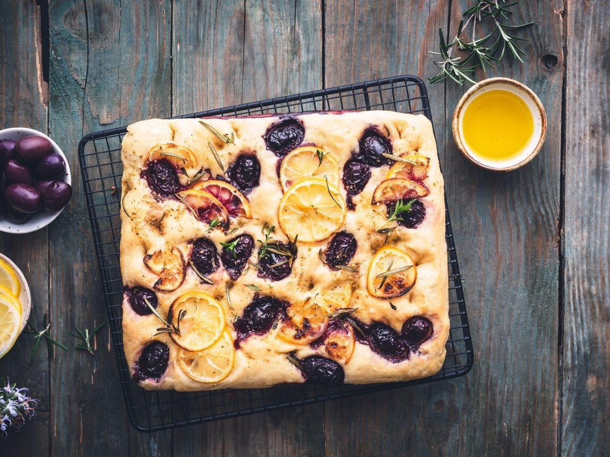 Zitronen-Focaccia mit Oliven, garniert mit Kräutern und serviert auf einem Küchenrost.