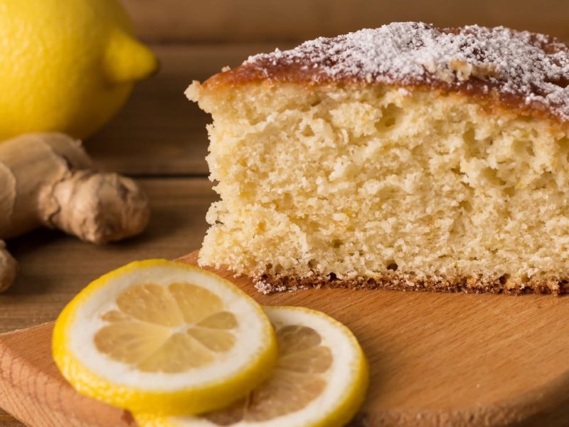 Ein Stück Kuchen auf einem Holzbrett mit Zitronenscheiben und Ingwer.