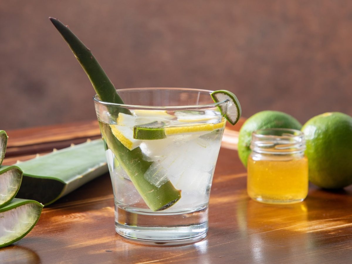 Ein Glas mit dem Aloe Vera-Fruchtfleisch, Limetten und Honig auf einem hellen Holztisch.