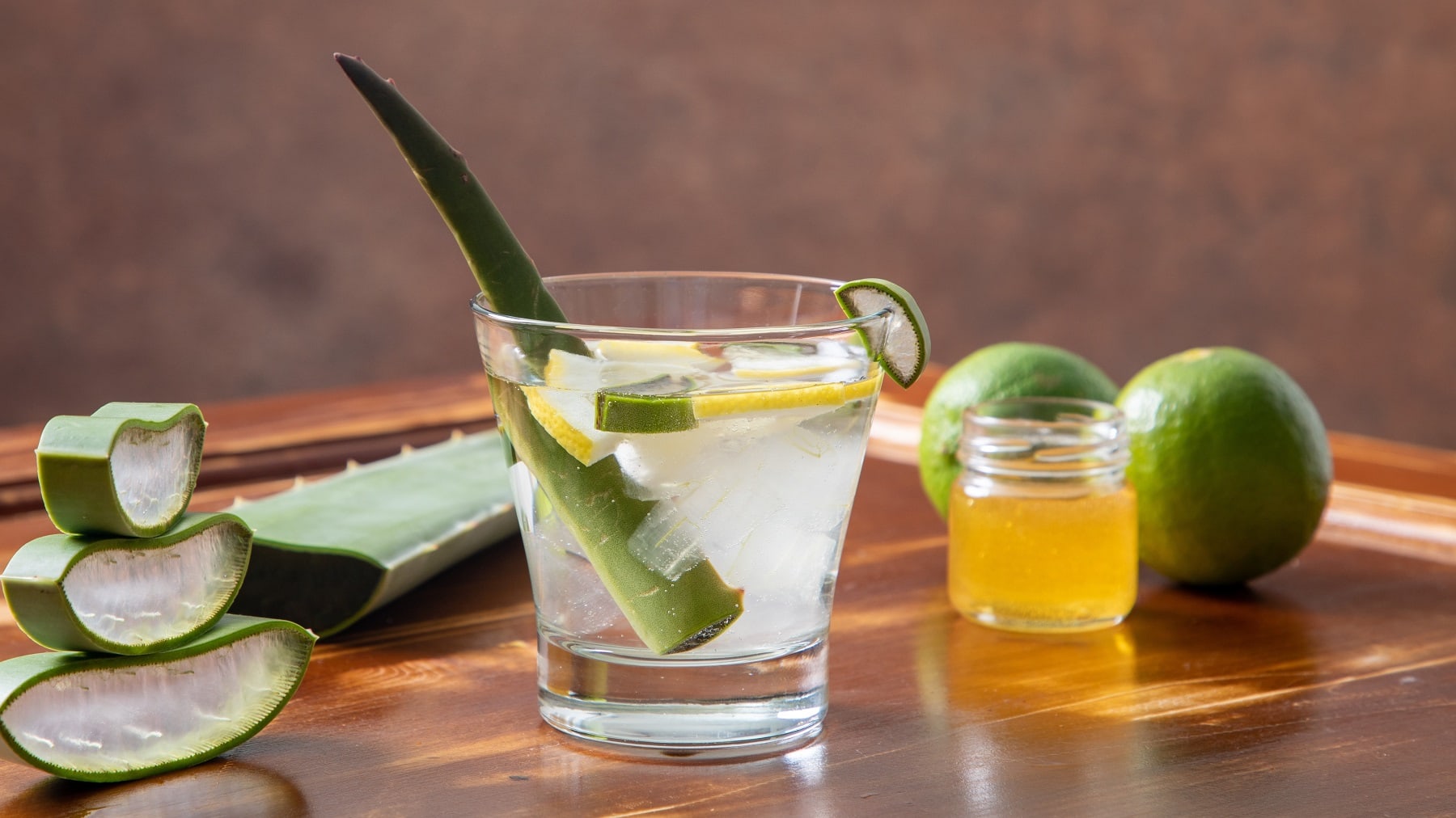 Ein Glas mit dem Aloe Vera-Fruchtfleisch, Limetten und Honig auf einem hellen Holztisch.