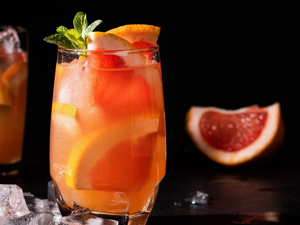 Zwei Gläser mit dem Aperol Paloma auf einem dunklen Tisch mit schwarzem Hintergrund.