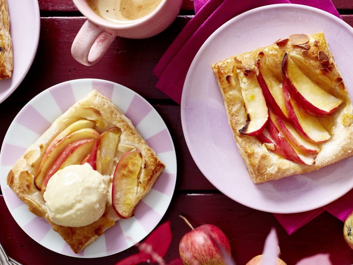 Apfel-Knusper-Teilchen mit Vanilleeis auf rosa Tellern vor Holzhintergrund in der Draufsicht.