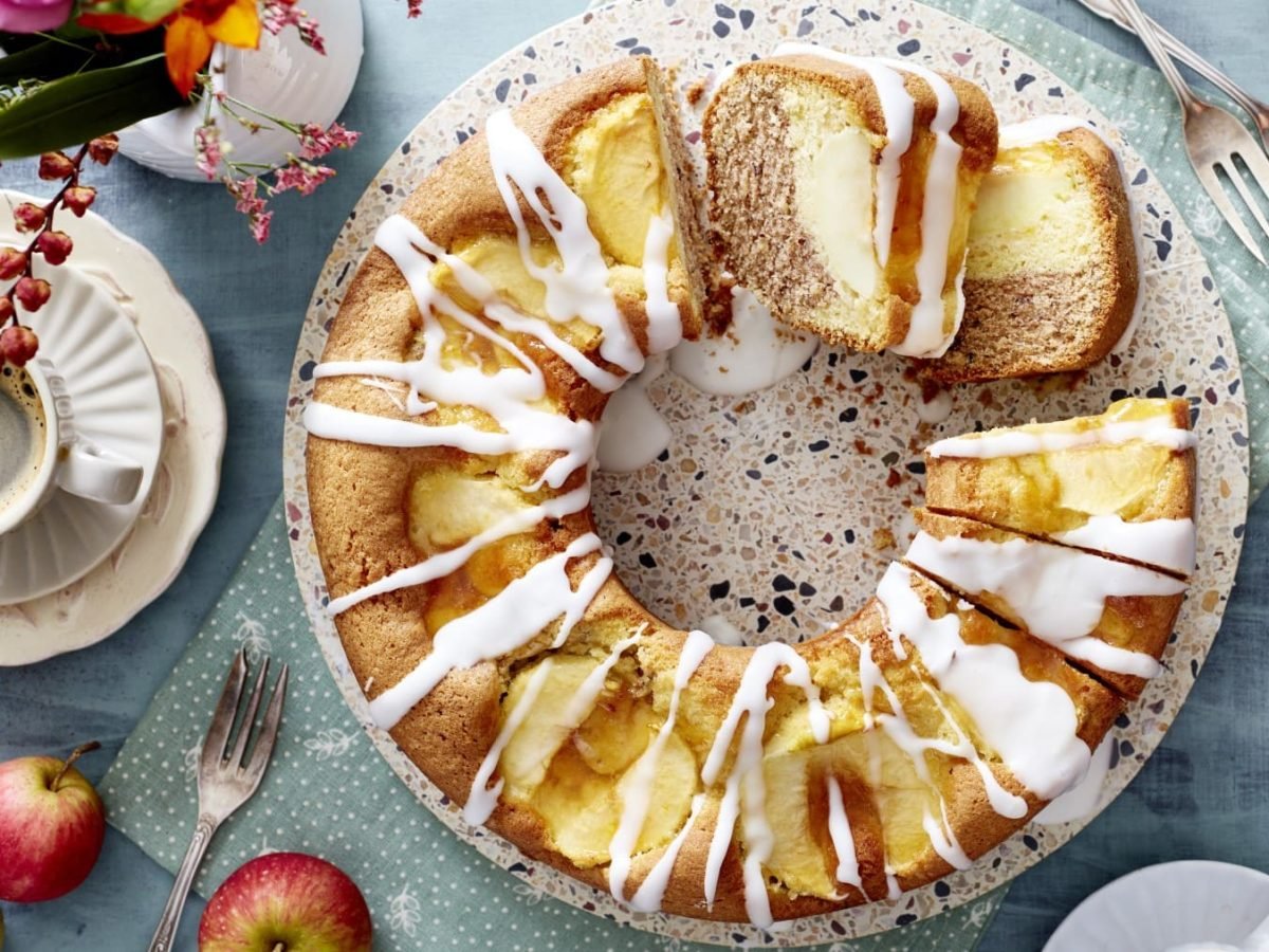 Auf einem Teller liegt Apfel-Kranzkuchen. Er ist mit Zuckerguss überzogen und mit Äpfeln gefüllt.