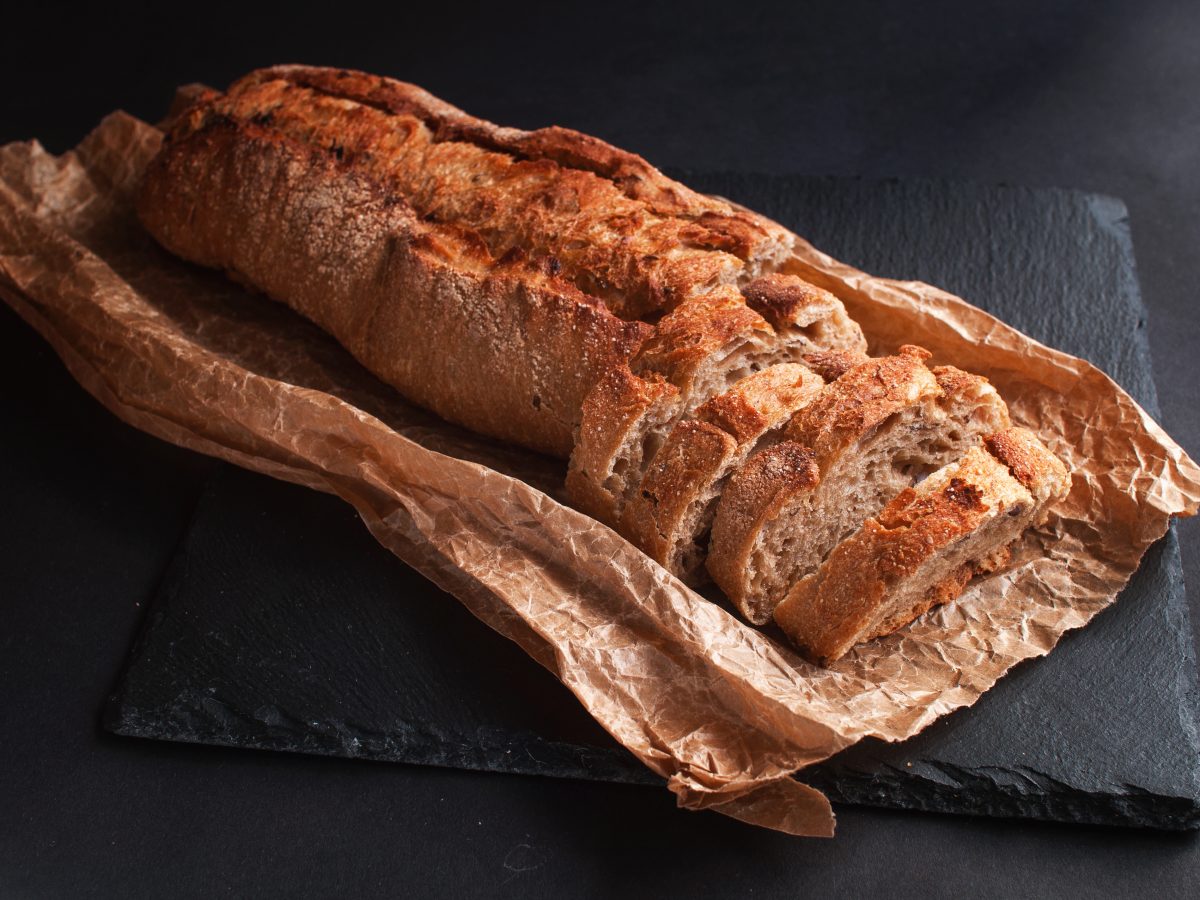 Angeschnittenes Baguette auf einer Papiertüte und einer Schieferplatte.