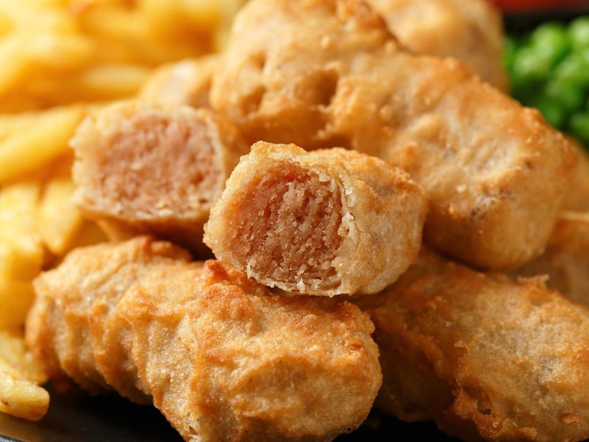 Irische Beer-Battered Sausages mit Pommes und Erbsen auf Teller. Frontalansicht.