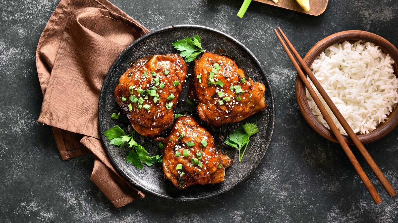 Einen schwarzen Teller mit Caramel Coco Chicken auf einem grauen Steintisch.