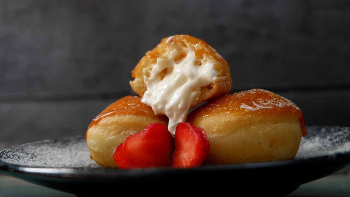 Drei Krapfen auf einem dunklen Teller und dunklem Hintergrund mit Erdbeeren dekoriert.