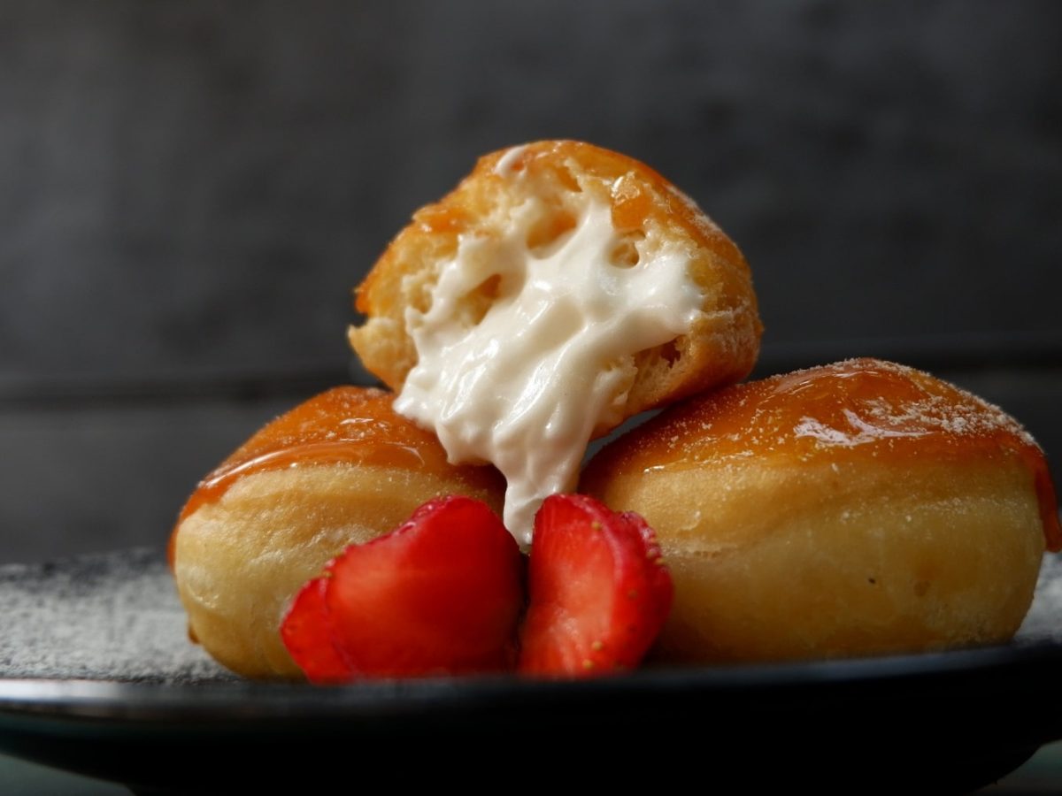 Drei Krapfen auf einem dunklen Teller und dunklem Hintergrund mit Erdbeeren dekoriert.