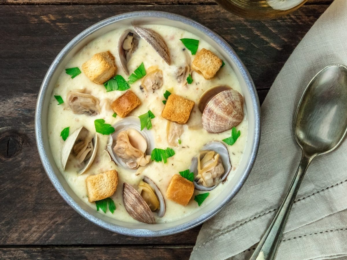 Eine graue Schale mit der Muschelsuppe auf einem dunklen Holztisch.