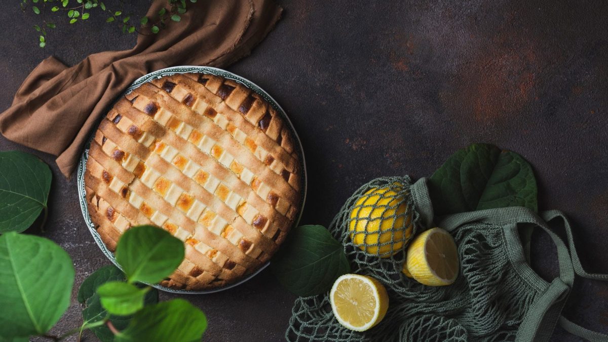 Crostata al limone in Springform auf dunklem Untergrund. Im Bild verteilt Zutaten.