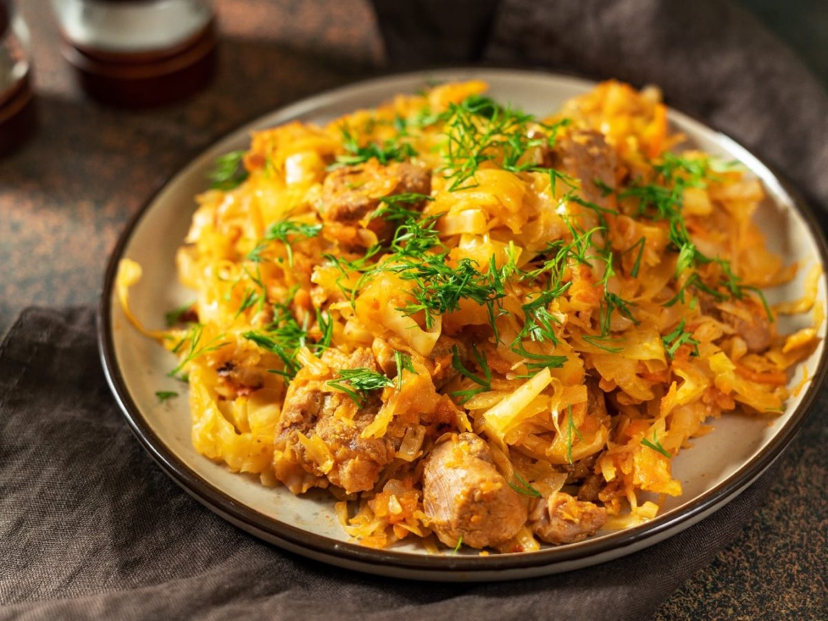 Ein weißer Teller mit schwarzem Rand, darauf der Curry-Kohl. Alles auf dunklem Untergrund mit einer goldenen Gabel.