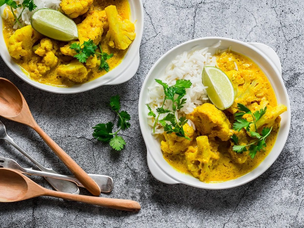 Zwei tiefe Teller mit Bananen-Curry mit Blumenkohl auf einem grauen Tisch.