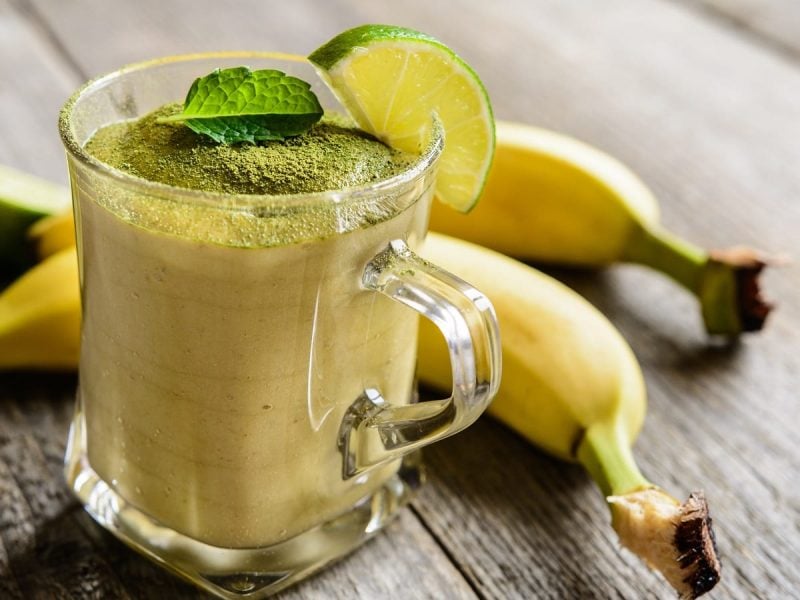 Ein Glas mit Bananen-Matcha-Smoothie auf einem Holztisch.