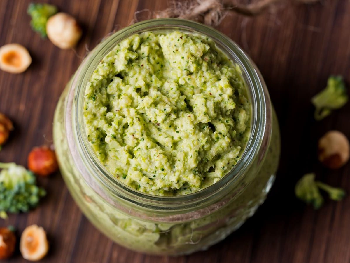 Ein Glas mit Brokkoli-Pesto auf einem braunem Holztisch.