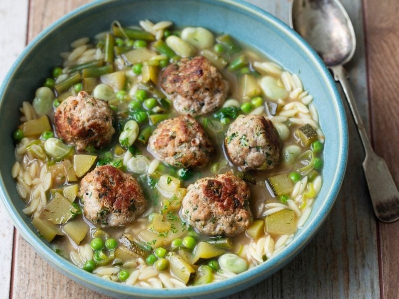 Ein tiefer blauer Teller mit grüner Minestrone auf einem Holztisch.