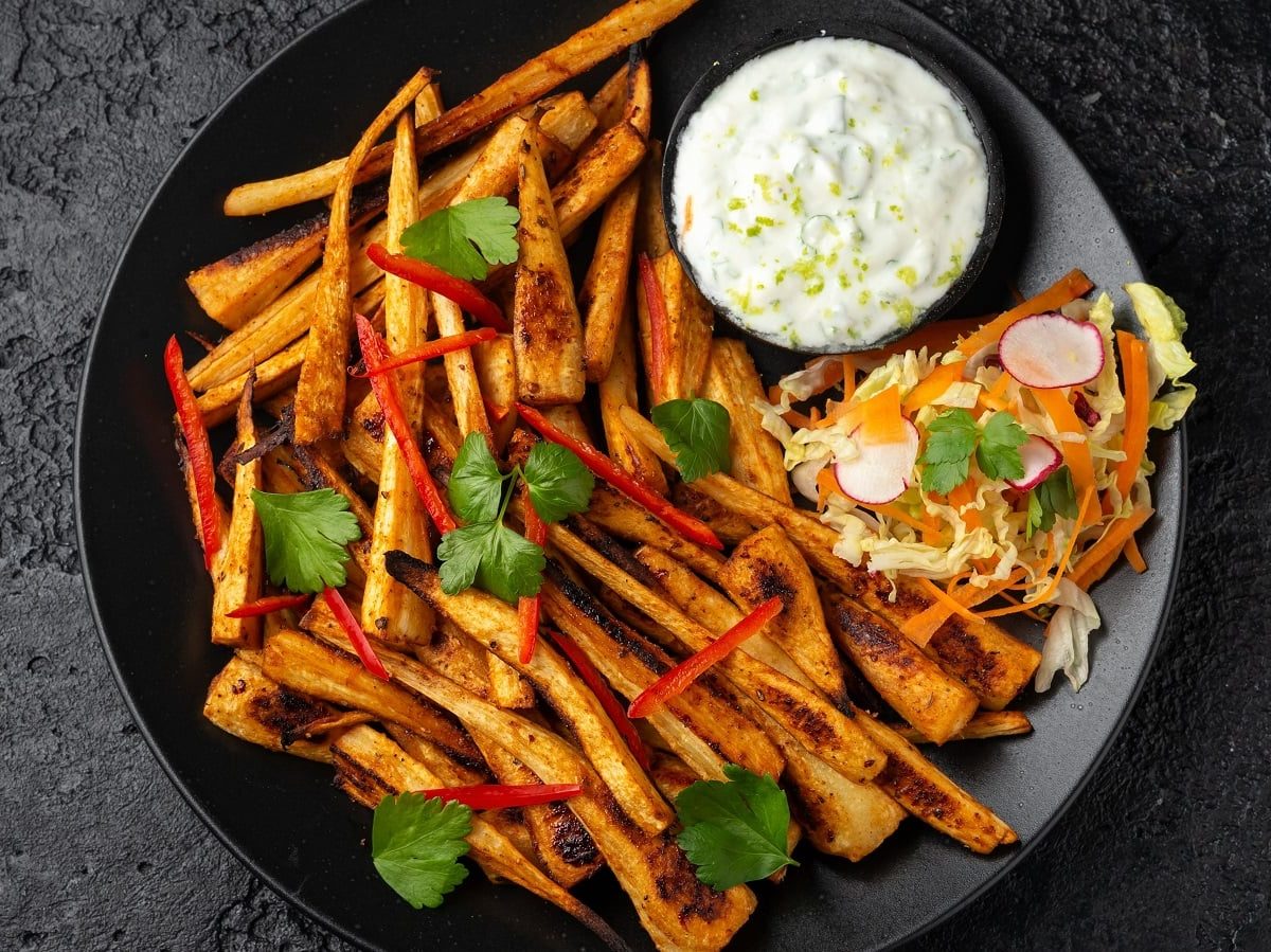 Ein schwarzer Teller mit Harissa-Pastinaken mit Knoblauch-Dip.