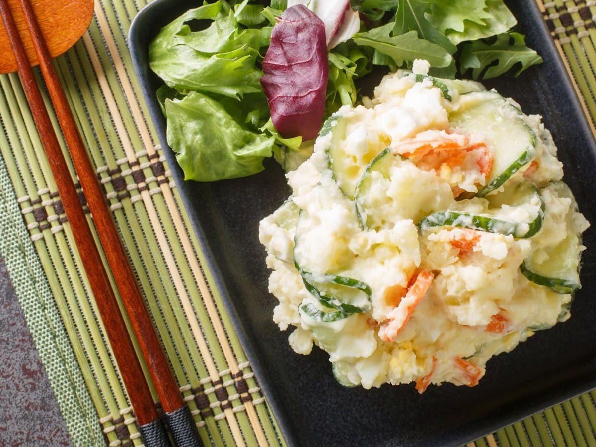 Ein schwarzes Tablett mit japanischer Kartoffelsalat auf einer Bambusmatte.