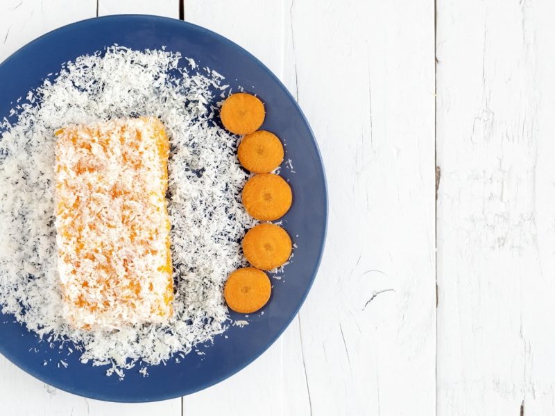 Ein blauer Teller mit einem Stück Kokos-Karottenkuchen darauf.