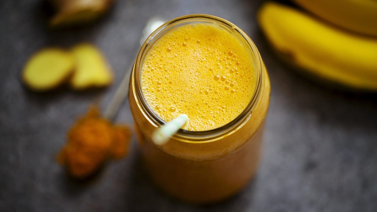 Ein Glas mit goldenem Smoothie neben frischen Früchten.