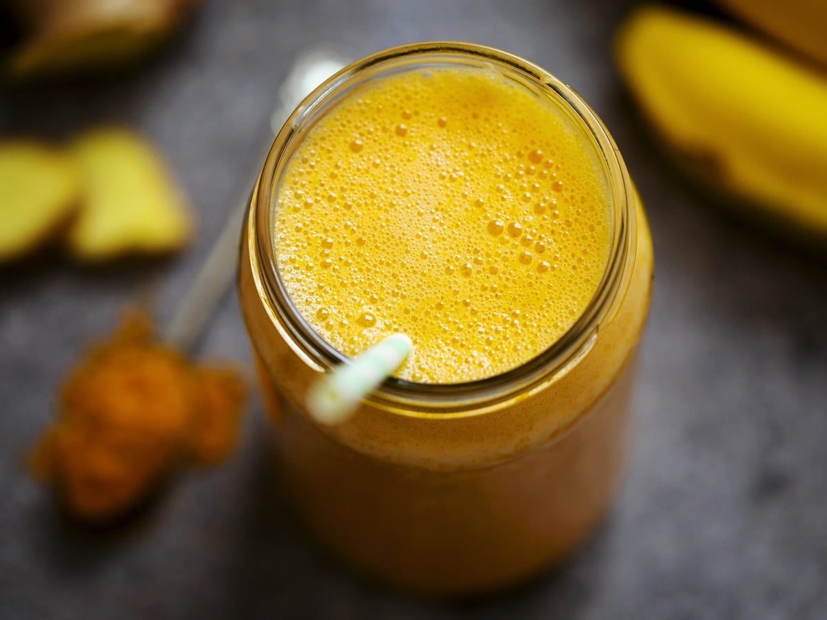 Ein Glas mit goldenem Smoothie neben frischen Früchten.