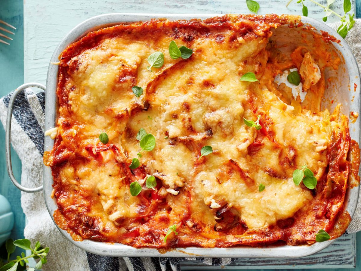 Hähnchen-Lasagne mit Paprika in der Draufsicht auf einem Küchentuch vor hellblauem Untergrund.