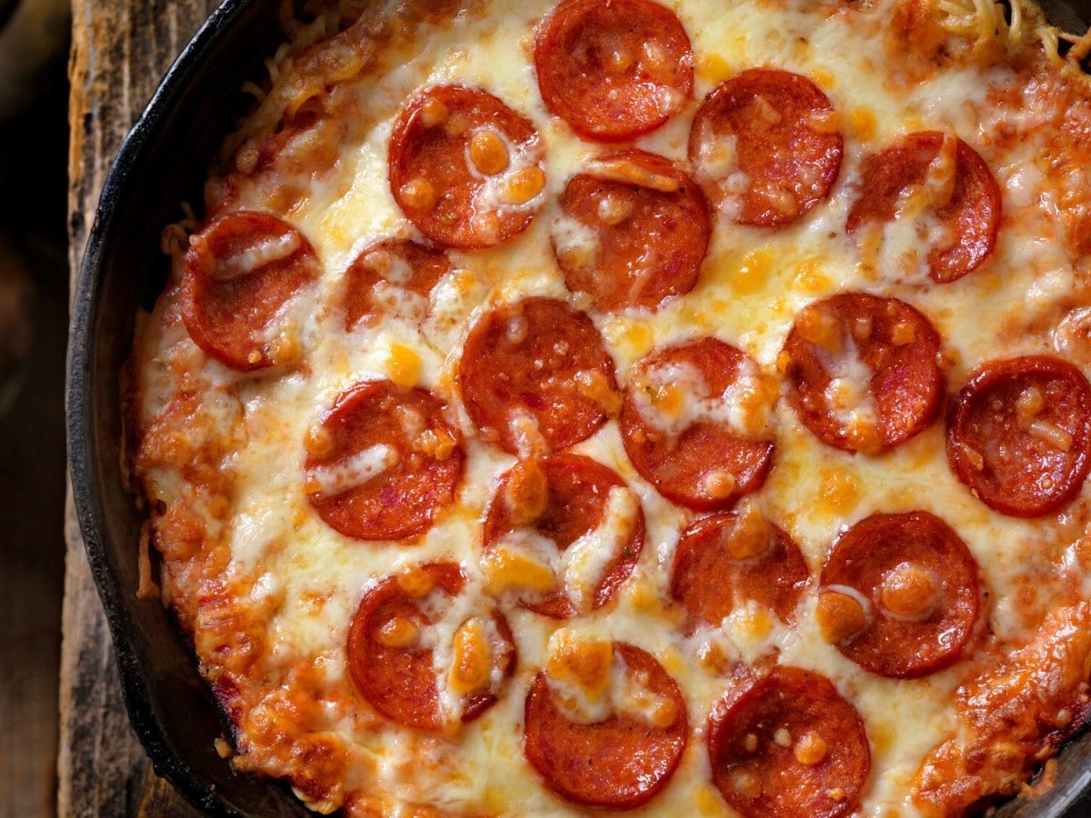 Instant Ramen Pizza in schwarzer Gusspfanne auf Holz. Daneben Salz- und Pfefferstreuer. Draufsicht.