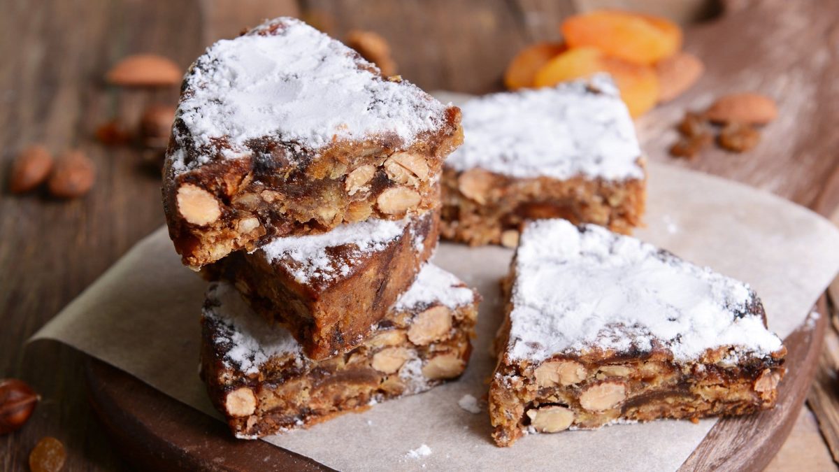 Frontalsicht: mehere Stücke Panforte liegen gestapelt auf einem Holztisch. es handelt sich um einen italienischen Kuchen.