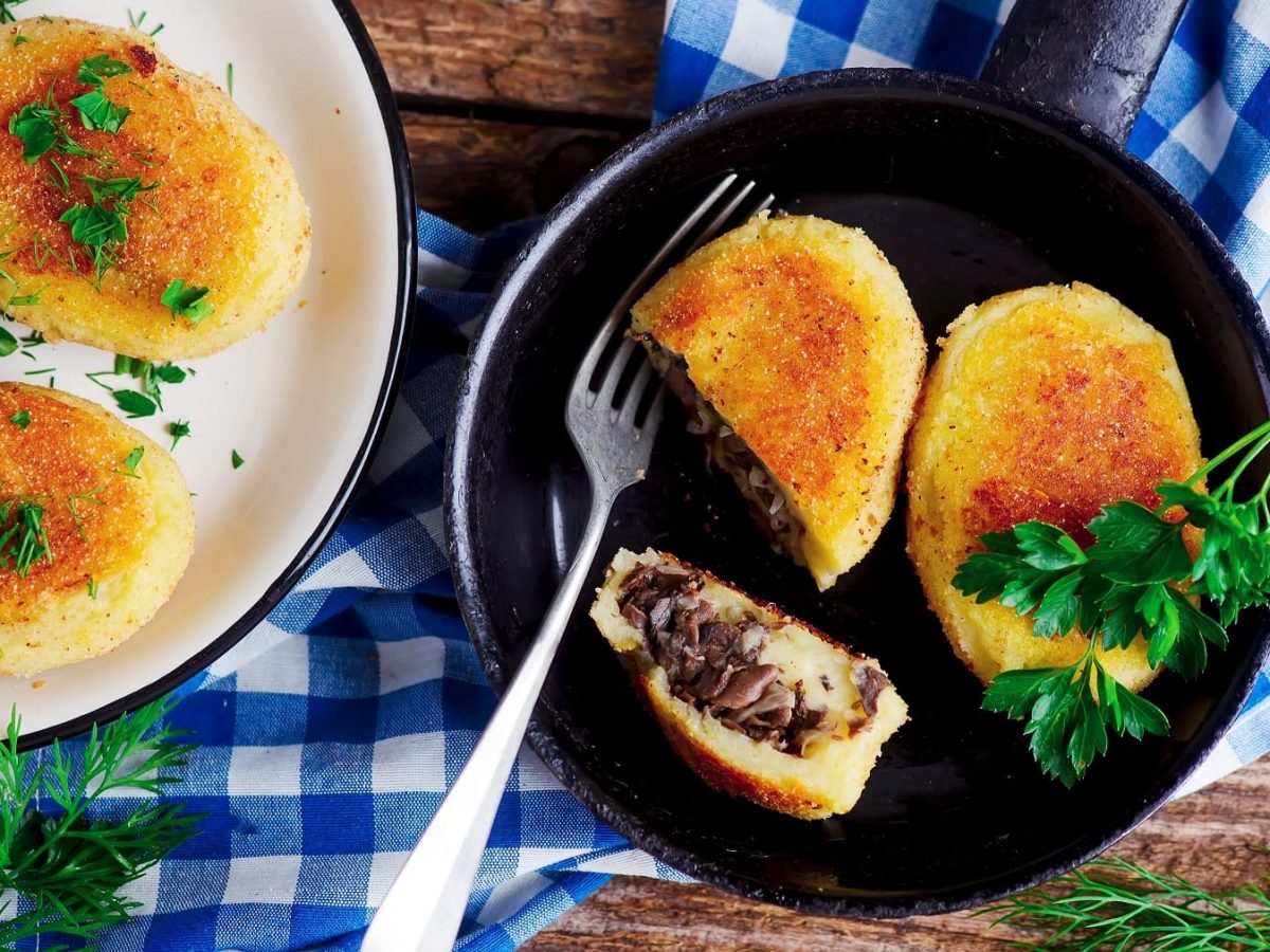 Eine Pfanne mit den Kartoffeltalern auf einem rustikalen Holztisch mit blau-weiß-karierter Tischdecke und Kräutern.