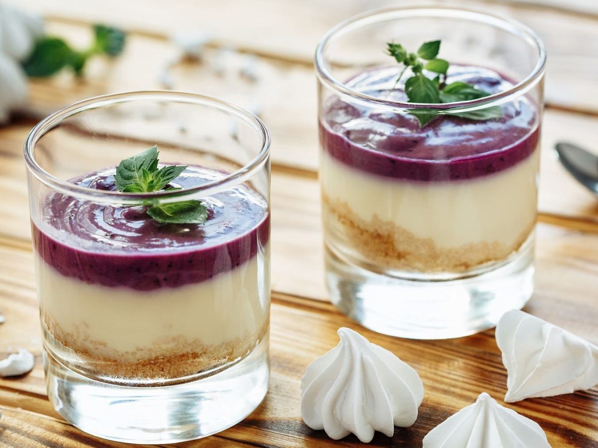 Zwei Gläser mit der Mandel-Panna-Cotta auf einem Holztisch mit zwei silbernen Löffeln.