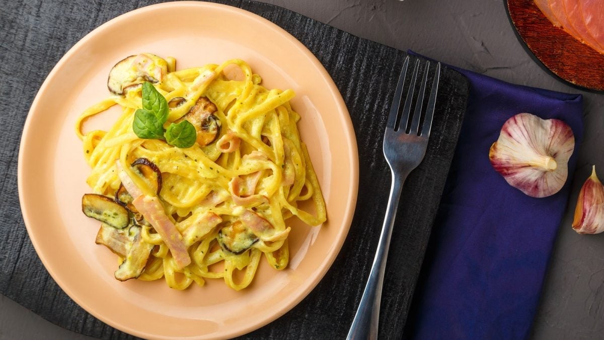 Ein runder rosafarbener Teller mit Miso Carbonara auf einem schwarzen Holzbrett.