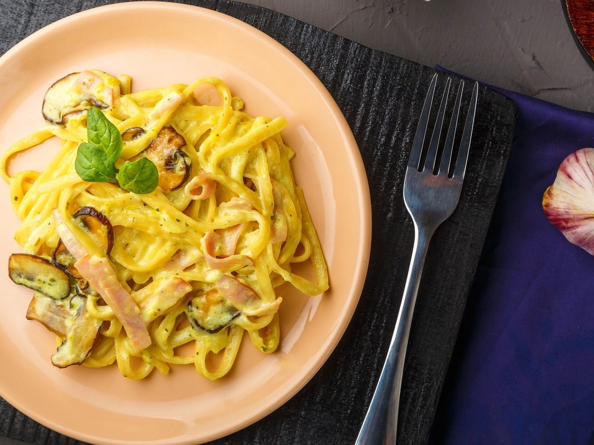 Ein runder rosafarbener Teller mit Miso Carbonara auf einem schwarzen Holzbrett.