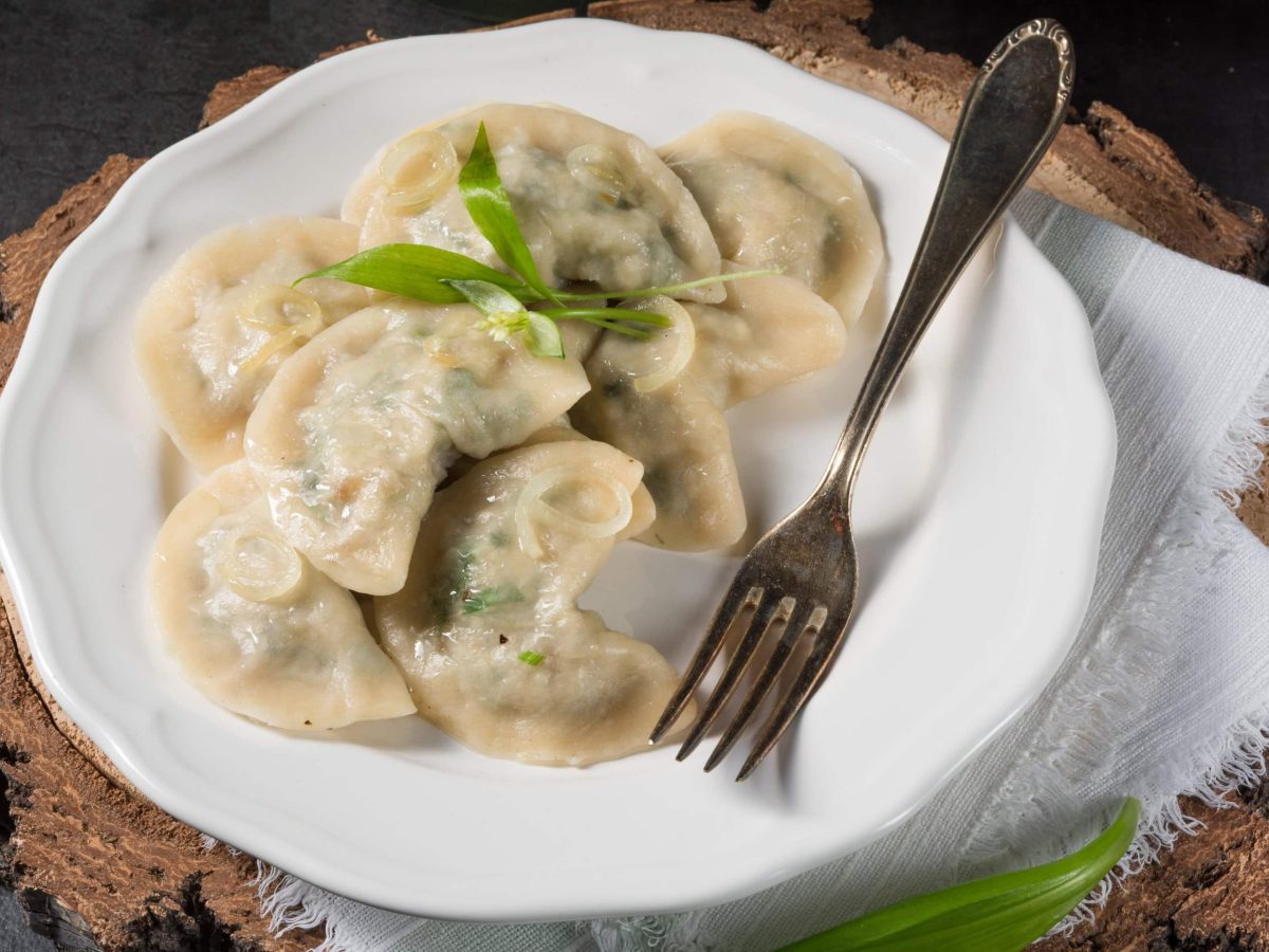 Draufsicht: Ein Teller Bärlauch-Maultaschen steht auf einem dunklen Untergrund aus Holz